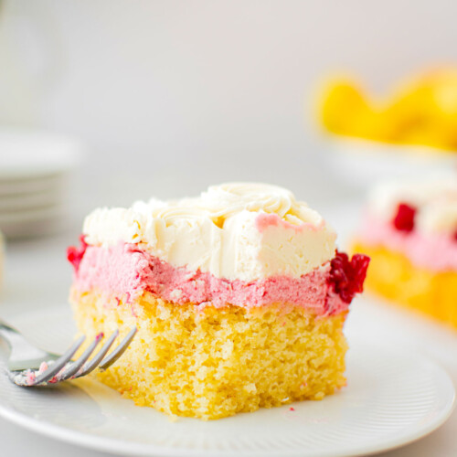 square slice of raspberry lemon snack cake on a cake plate with a fork and a bite taken out.