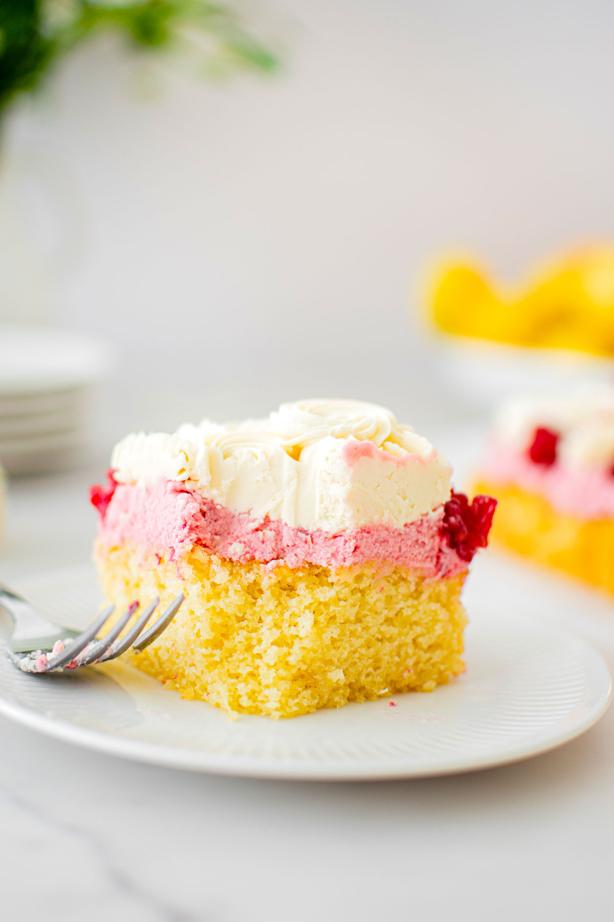 square slice of raspberry lemon snack cake on a cake plate with a fork and a bite taken out.