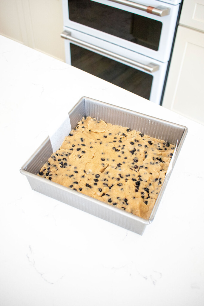 vegan blueberry bars pressed into a square baking pan on a white marble counter.