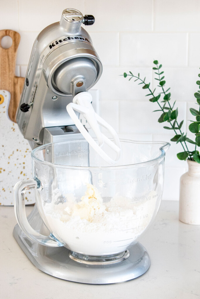 ingredients for vegan blueberry frosting in a stand mixer sitting on a white marble counter.