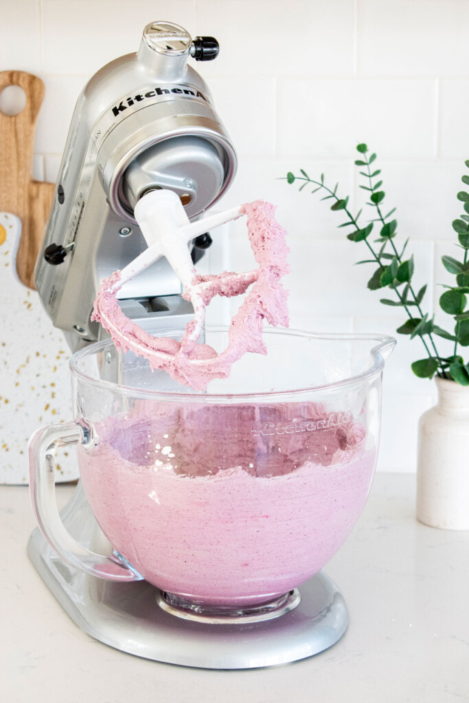 blueberry frosting in the bowl of a stand mixer on a white marble counter.