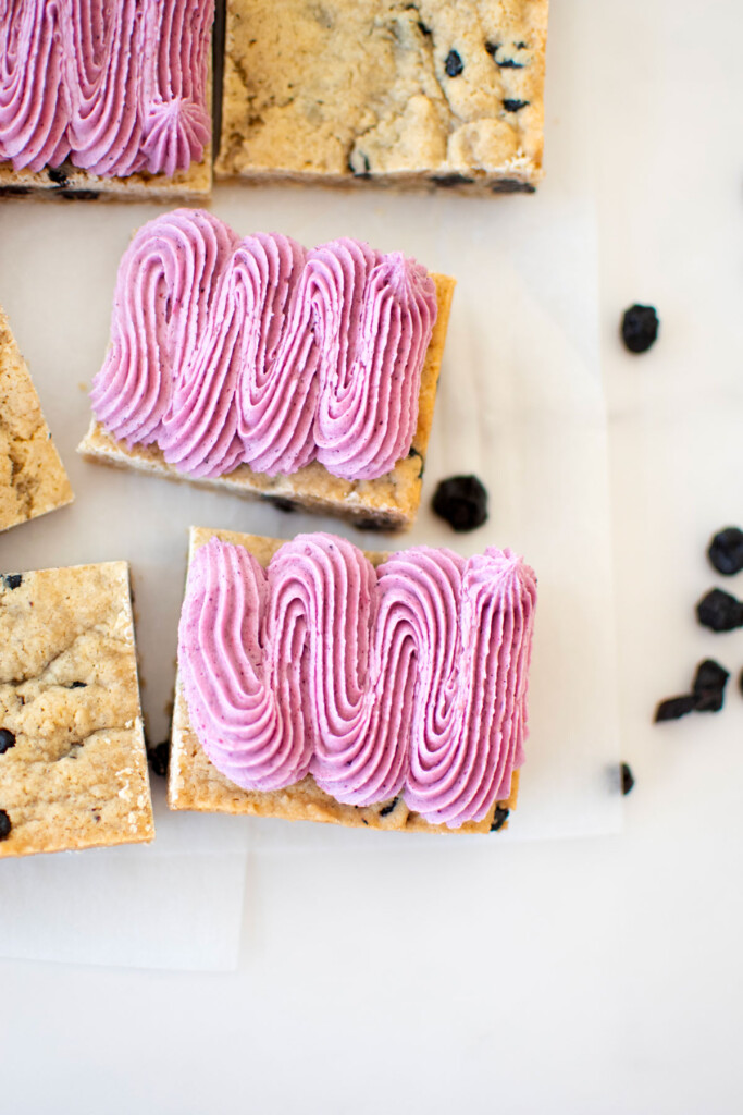 vegan blueberry bar with frosting on a white marble counter.