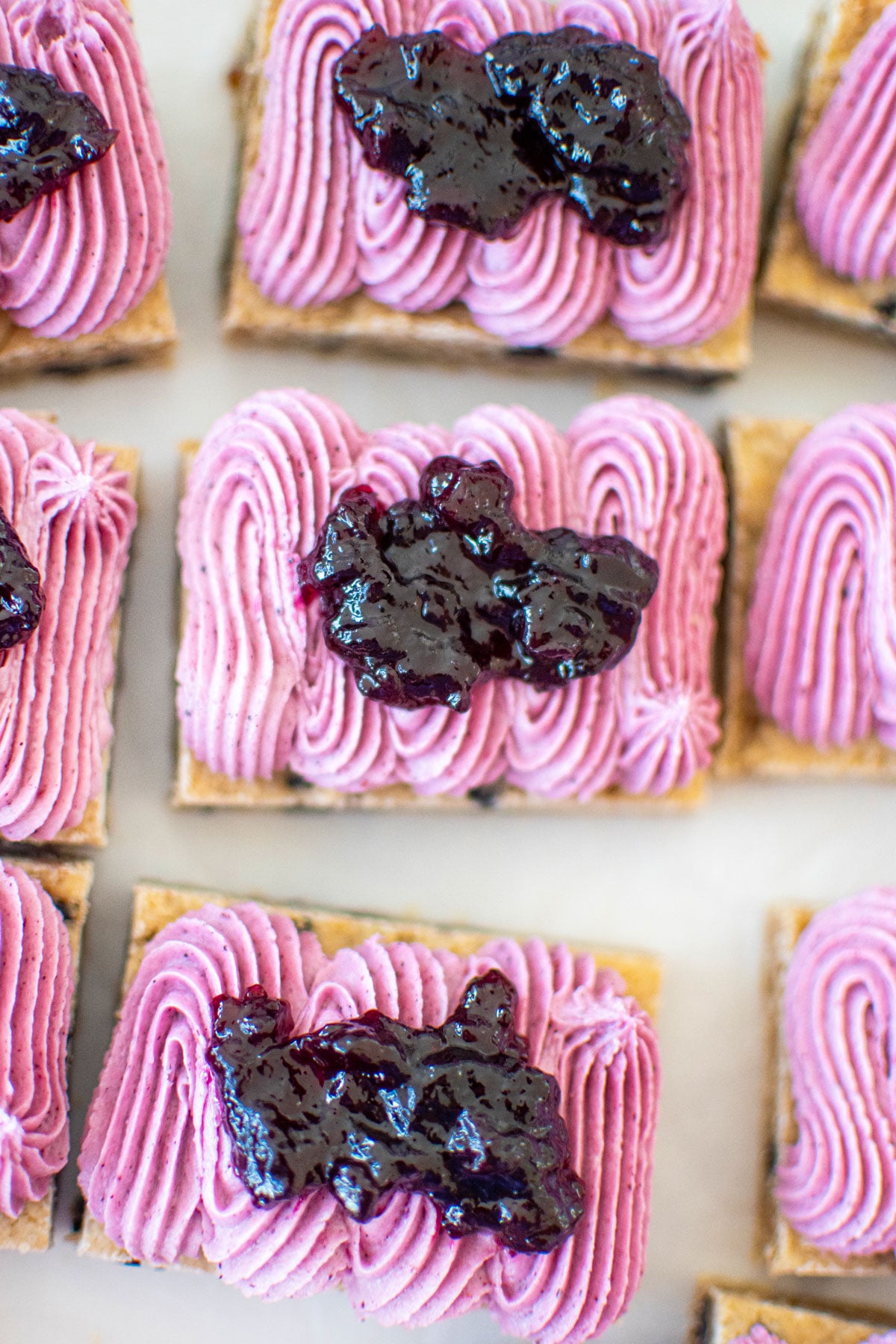 vegan blueberry bars with frosting and blueberry jam on a white marble counter.