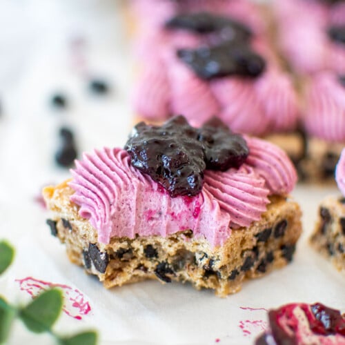 vegan blueberry bar with frosting and blueberry jam with a bite taken out on a white marble counter.
