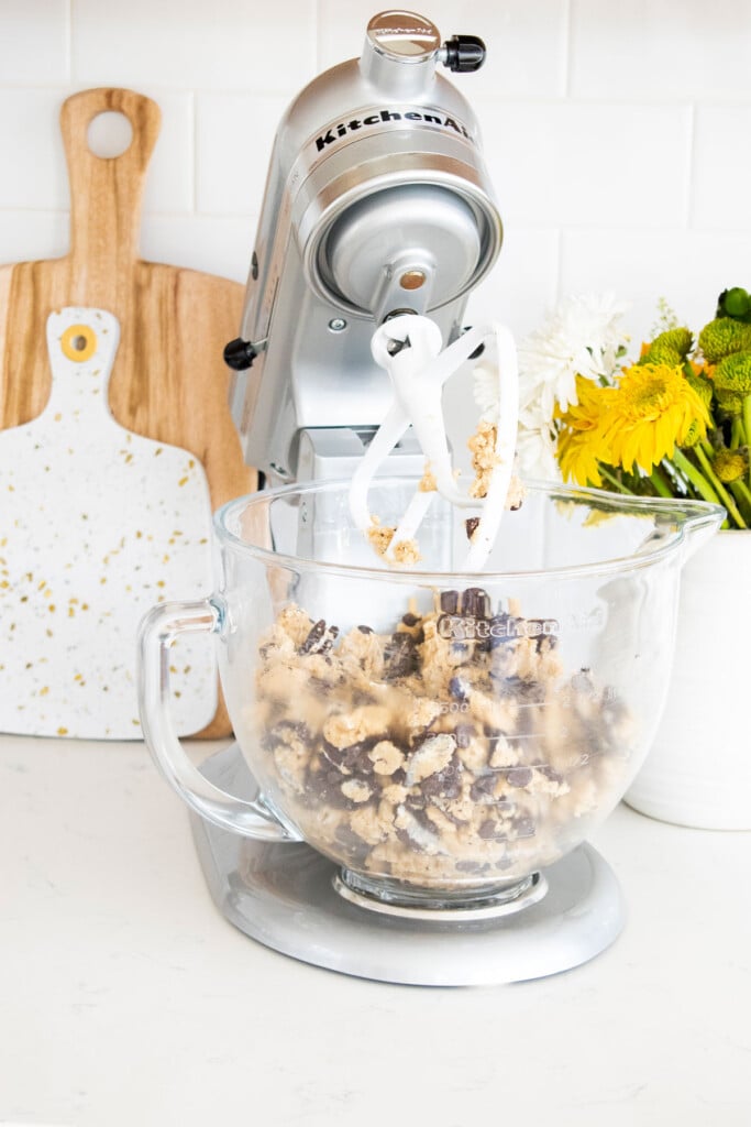 vegan oreo chocolate chip cookie dough in a stand mixer on a white marble counter with a vase of flowers.