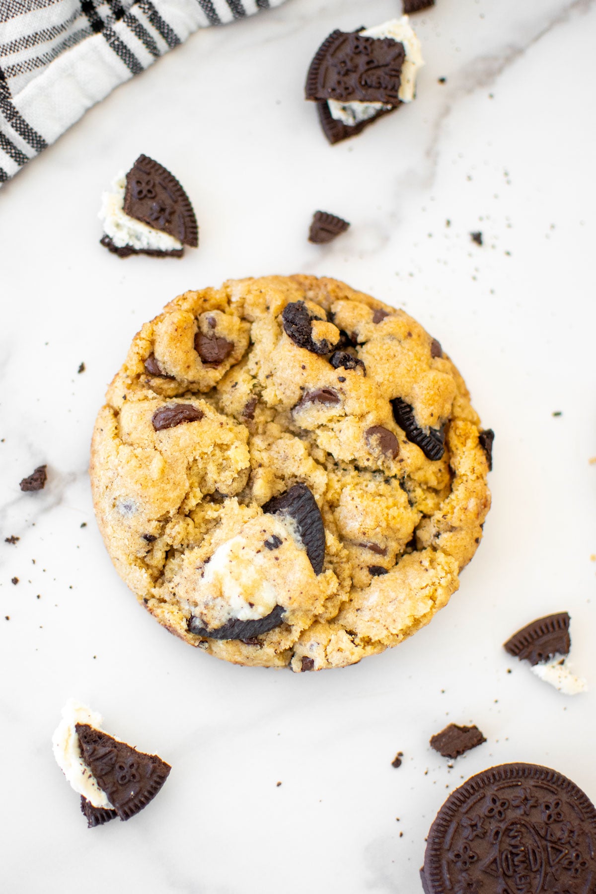 vegan oreo cookie on a white marble counter with broken oreo pieces all around.