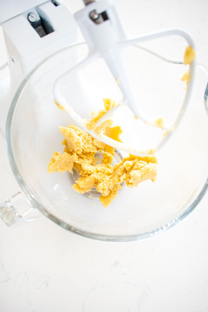 creamed butter and sugar in a glass mixing bowl on a white marble counter.