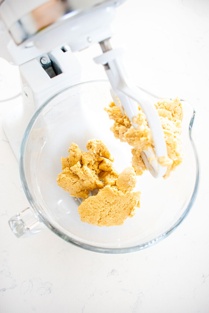 eggless sprinkle cookie dough in a glass mixing bowl on a white marble counter.