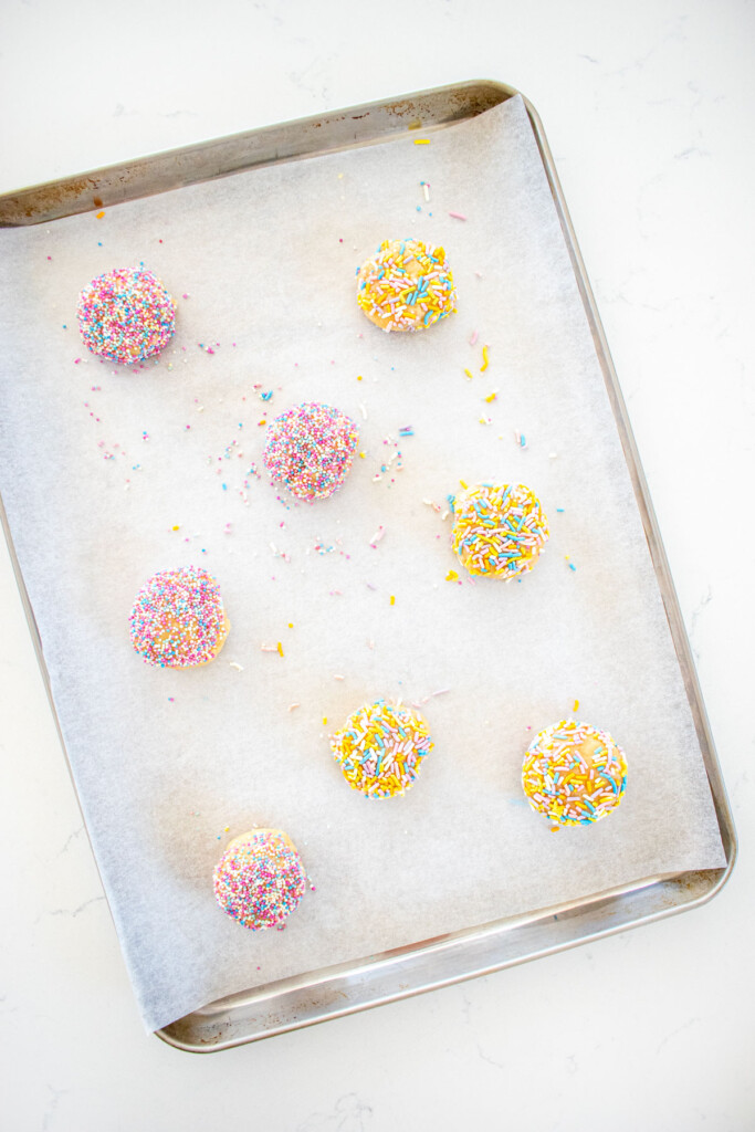 eggless sprinkle cookie dough balls on a baking sheet on a white marble counter.