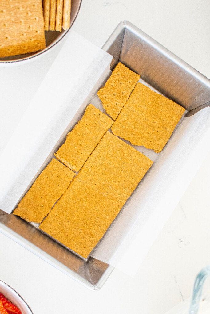 graham crackers broken into pieces in a 1 pound loaf pan on a white marble counter.