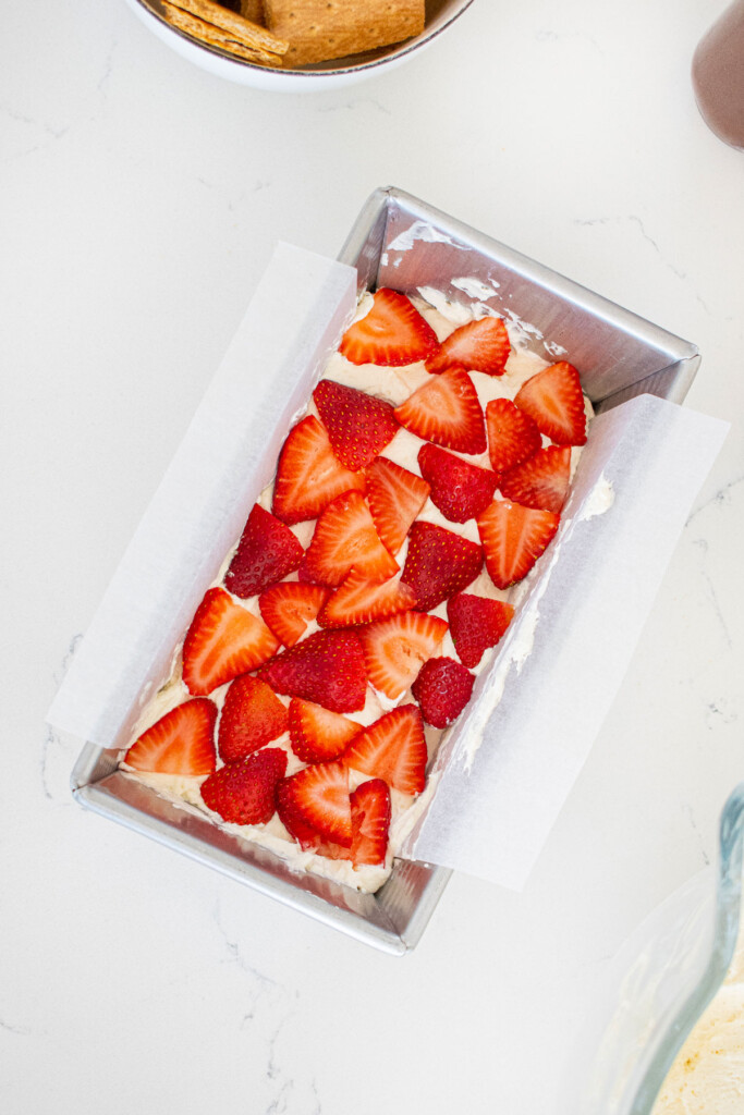 whipped cream spread evenly with strawberries slices in a 1 pound loaf pan on a white marble counter.