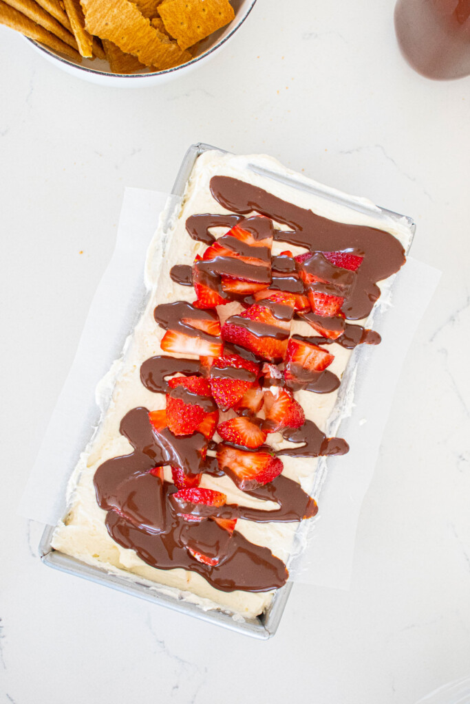 whipped cream spread evenly with strawberries slices and chocolate sauce drizzled in a 1 pound loaf pan on a white marble counter.