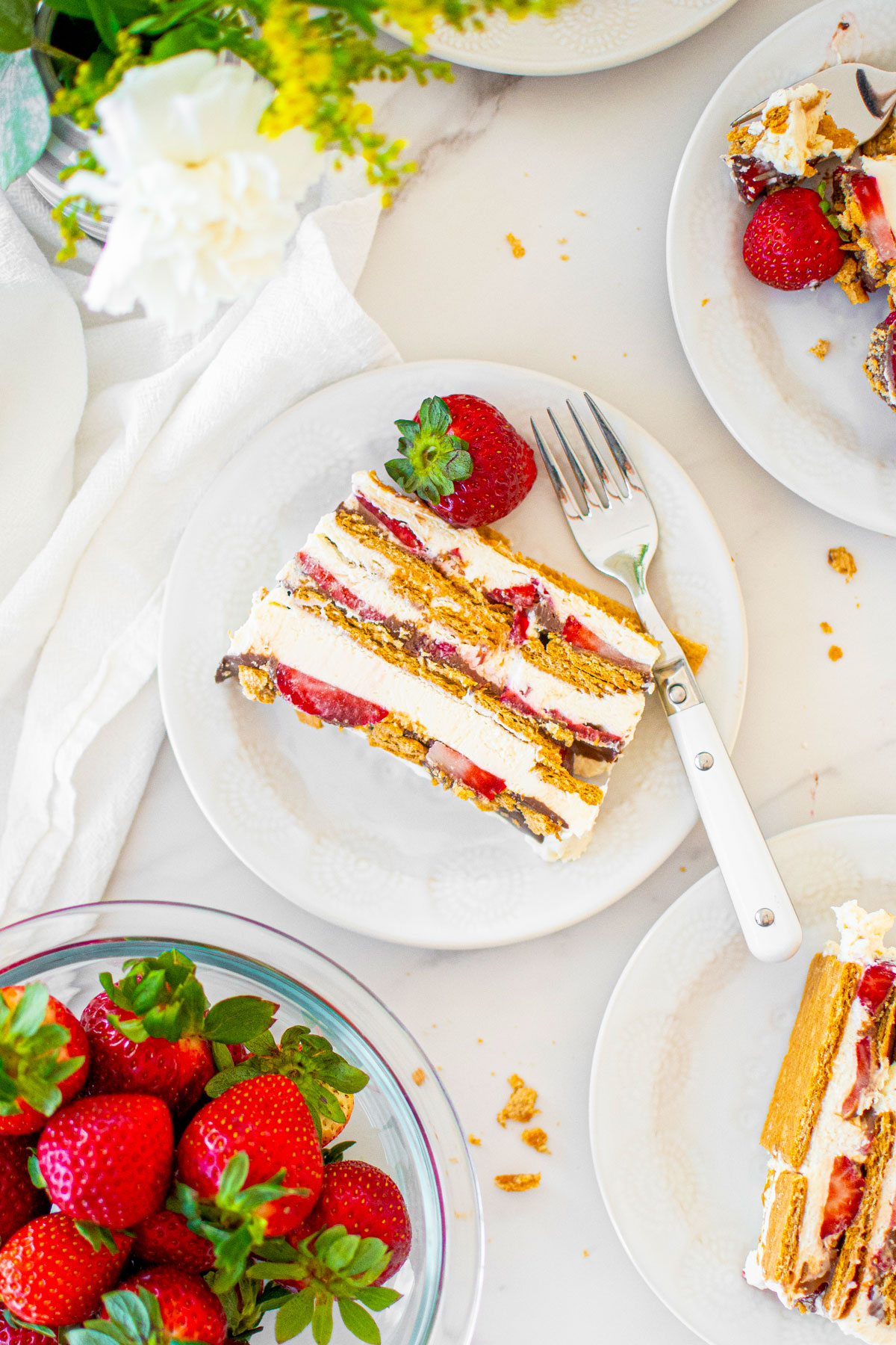 slice of neapolitan icebox cake on a white plate on a marble counter with fresh strawberries.