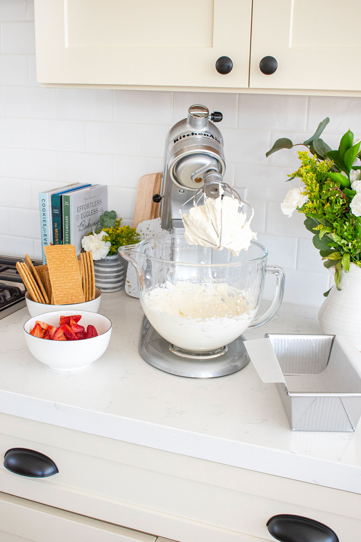 homemade whipped cream in a stand mixing bowl on a white marble counter.