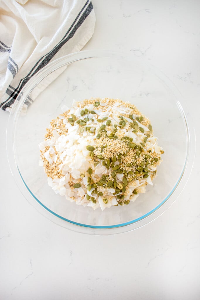 dry ingredients for pumpkin granola for dogs in a glass mixing bowl on a marble counter.