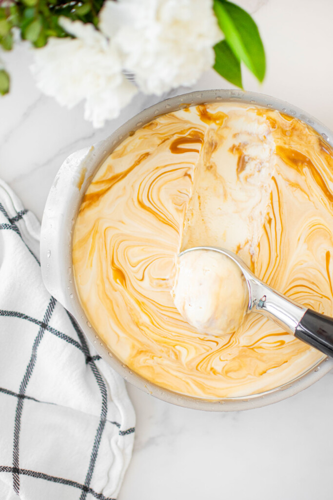 salted caramel no churn ice cream in a baking pan being scooped out on a white marble counter.