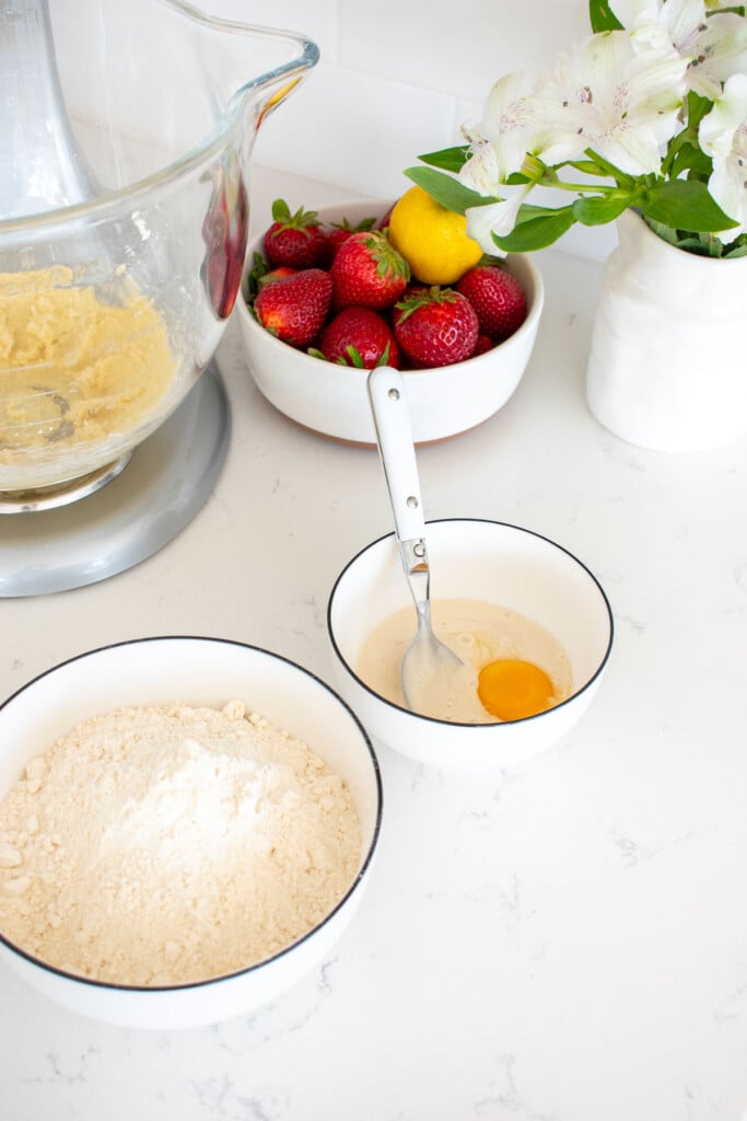 bowl of flour and a bowl of sourdough discard with egg yolk on a white marble countertop.