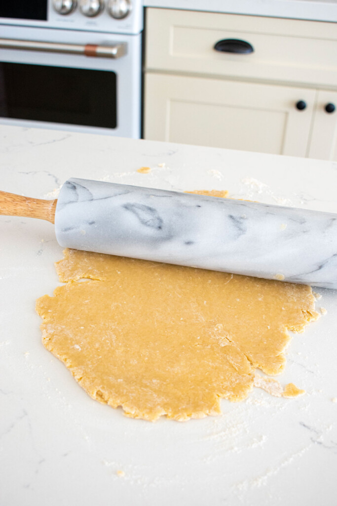 sourdough pop tart dough being rolled out on a white marble countertop.