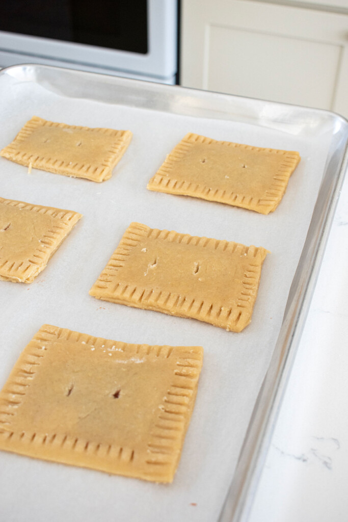 unbaked sourdough strawberry pop tarts on a baking sheet with crimped edges and vents.