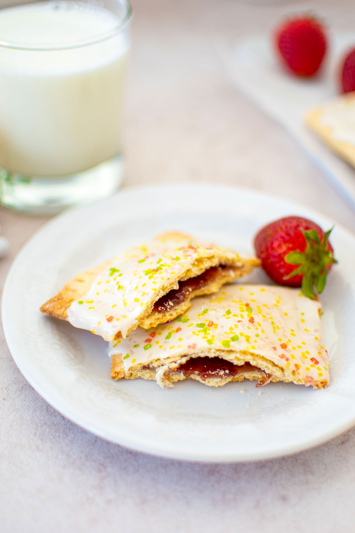 sourdough strawberry pop tart cut in half on a plate with a strawberry and a glass of milk.