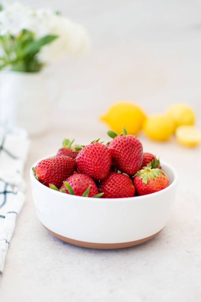 bowl of fresh strawberries on a light pink background with fresh lemons.