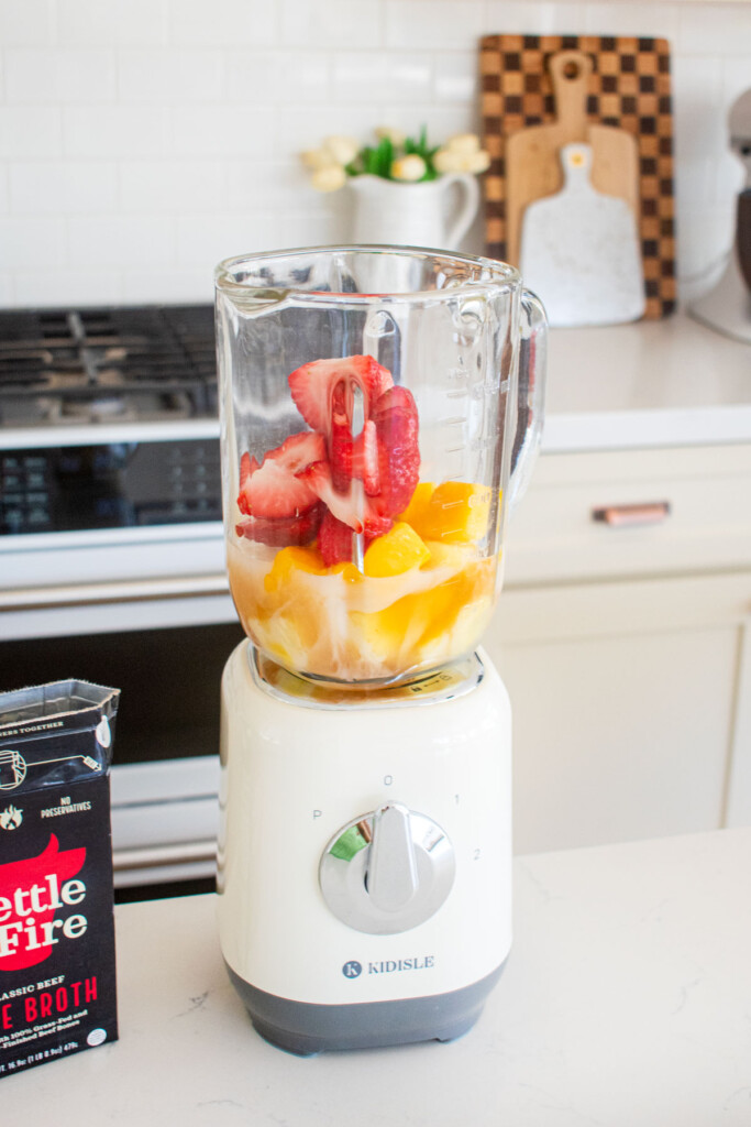 ingredients for tropical bone broth protein smoothie in a glass blender on a kitchen counter.