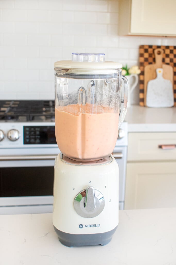 tropical bone broth protein smoothie blended in a blender on a white marble counter.