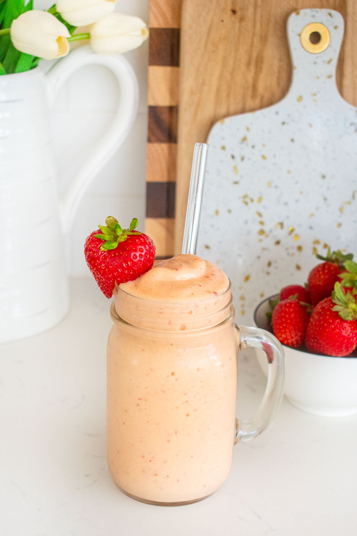 tropical bone broth protein smoothie with a fresh strawberry on the glass on a white marble counter with fresh strawberries.