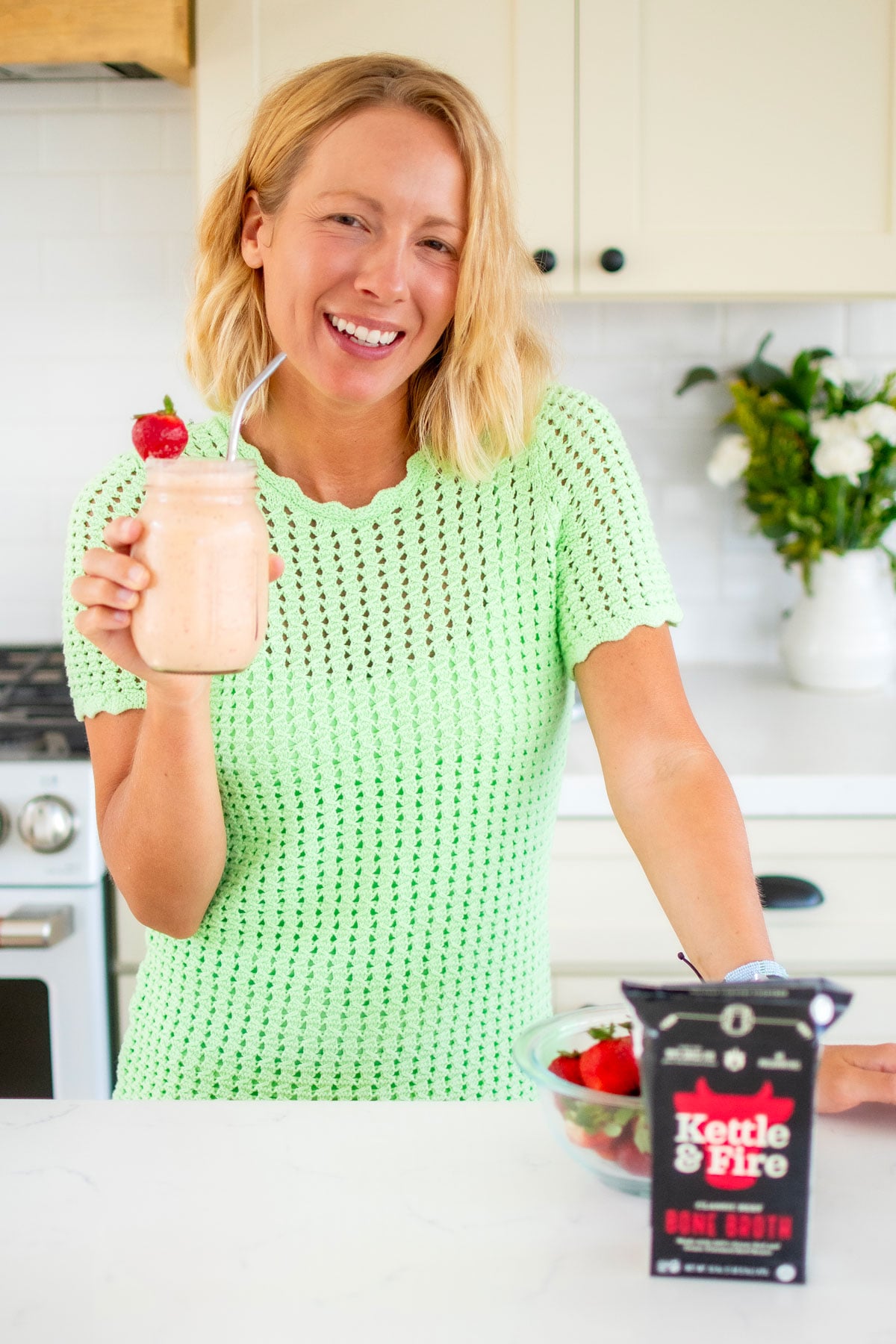 woman drinking a tropical bone broth smoothie standing at the kitchen counter.