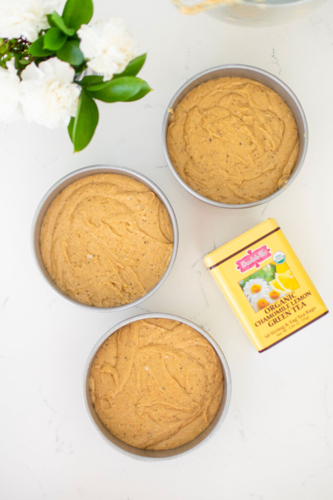 vegan lemon chamomile tea cake batter in three 6-inch cake pans on a white marble counter.