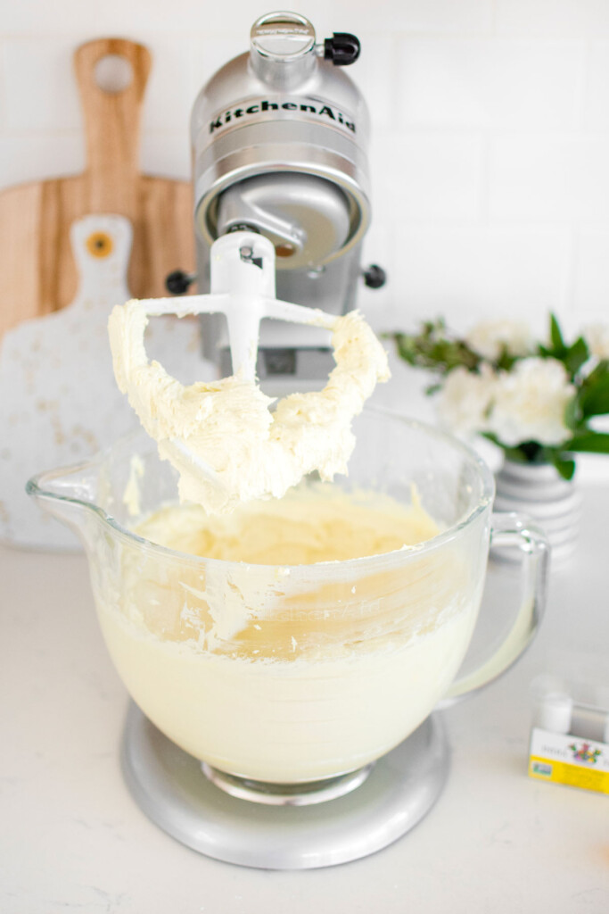 vegan lemon buttercream frosting in a glass stand mixing bowl on a white marble counter.