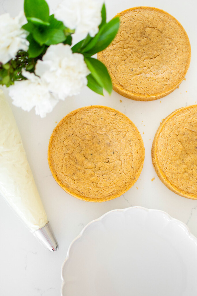 vegan lemon chamomile tea cake layers on a white marble counter with a piping bag of lemon frosting.