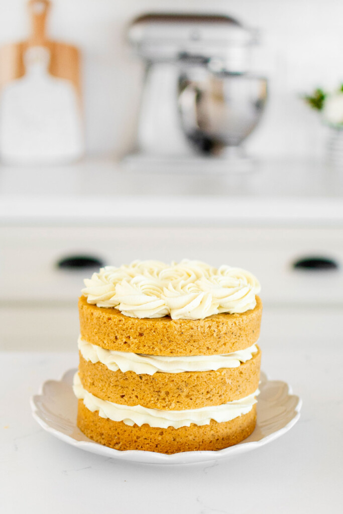 vegan lemon chamomile tea cake frosted on a cake plate on a white marble counter.