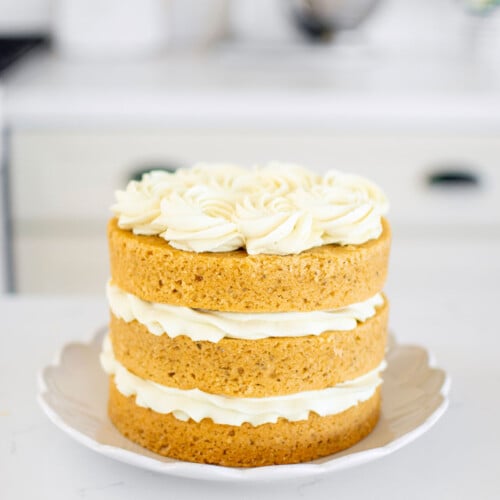 vegan lemon chamomile tea cake frosted on a cake plate on a white marble counter.