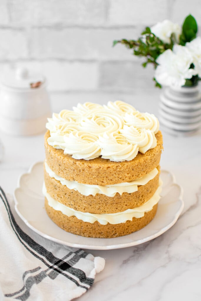 vegan lemon chamomile tea cake frosted on a cake plate on a white marble counter with fresh flowers.