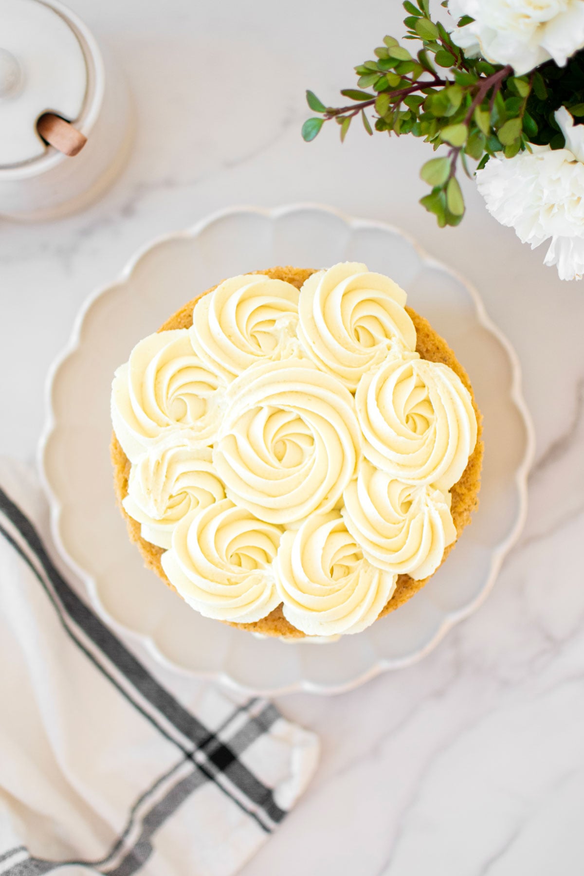 vegan lemon chamomile tea cake frosted with lemon buttercream rose frosting pm top on a white ruffle cake plate.