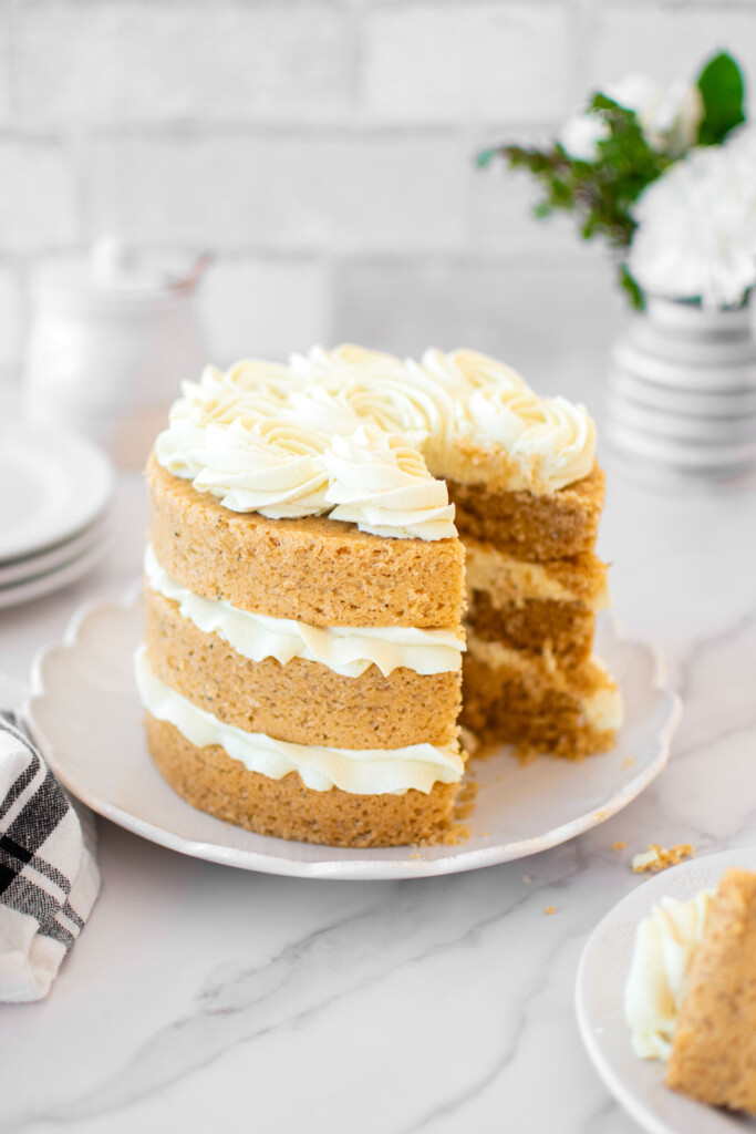 vegan lemon chamomile tea cake frosted on a cake plate on a white marble counter with fresh flowers.