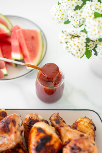 homemade bbq sauce with bone broth in a glass jar with a spoon on a white marble countertop,.