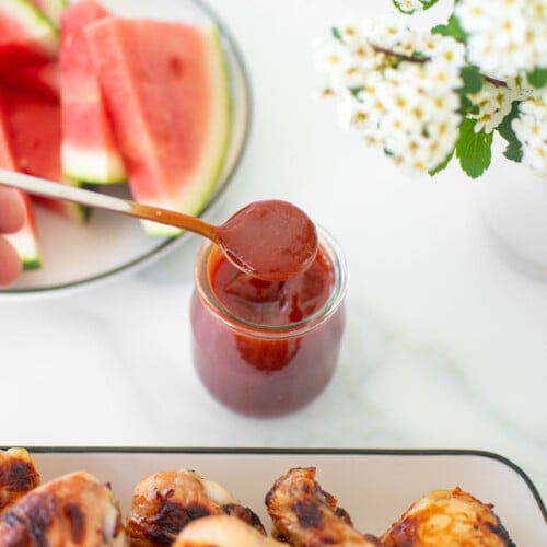 homemade bbq sauce with bone broth in a glass jar with a spoon on a white marble countertop,.
