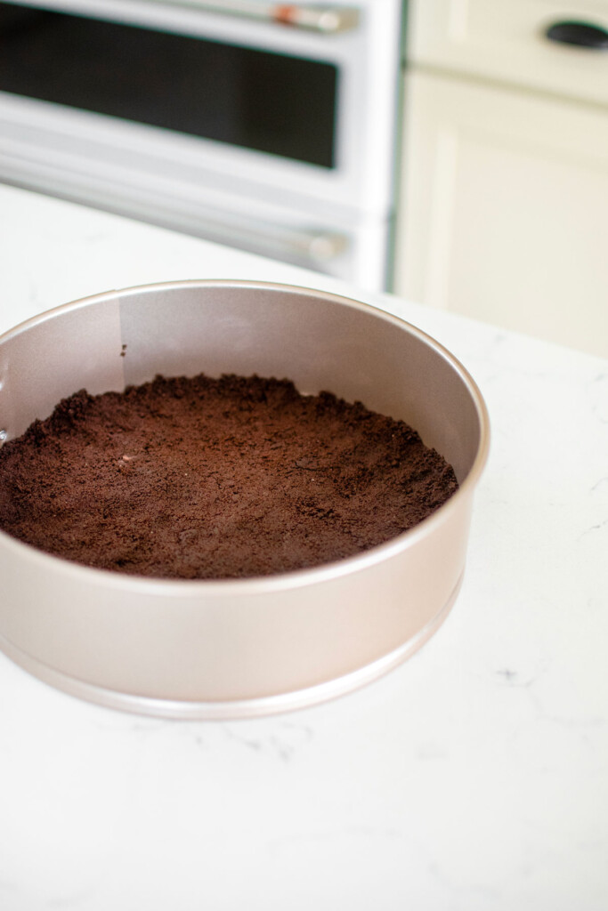 chocolate graham cracker crust in a springform pan on a kitchen counter.