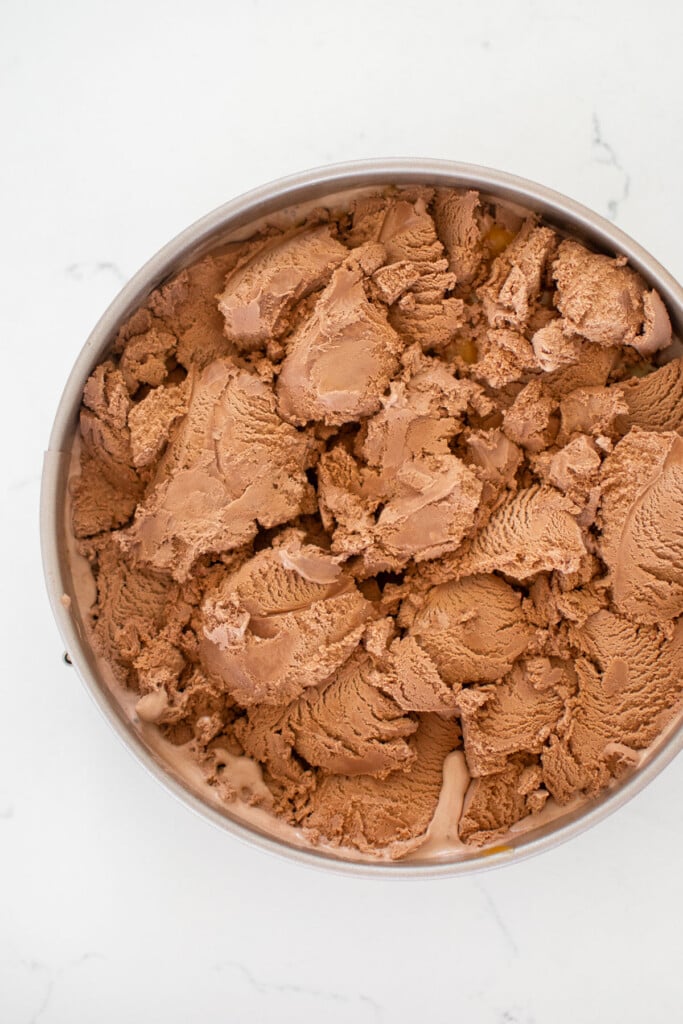 chocolate banana caramel ice cream pie being assembled on a white marble counter.