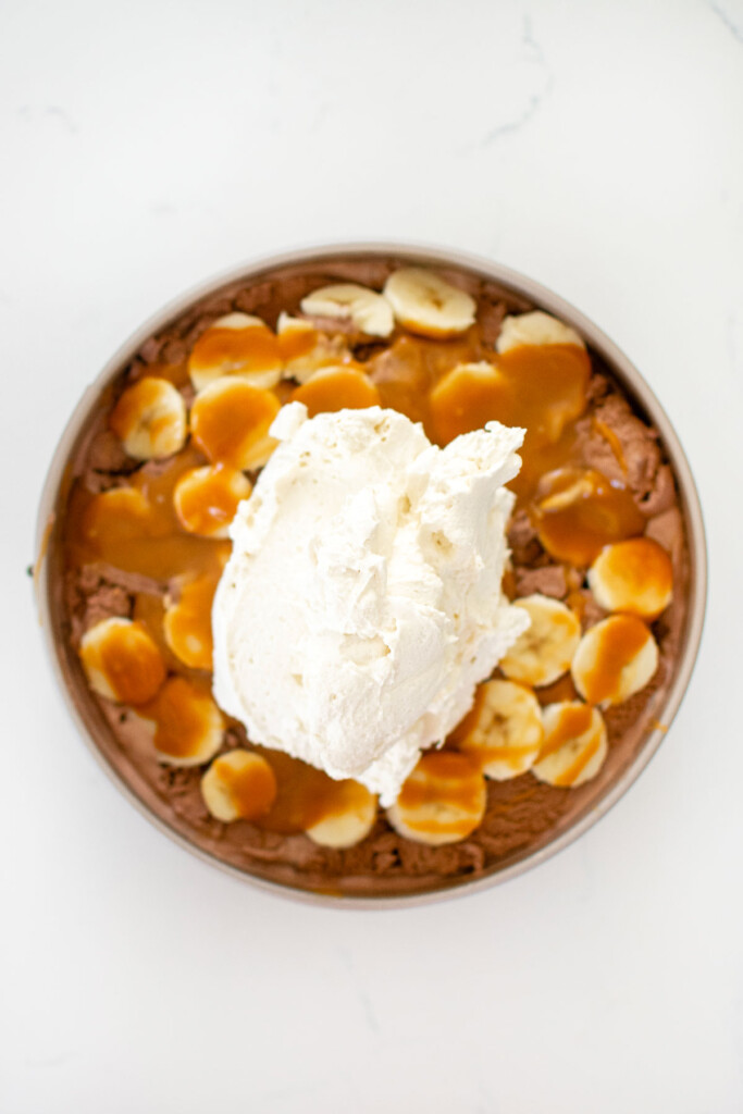 chocolate banana caramel ice cream pie being assembled on a white marble counter.