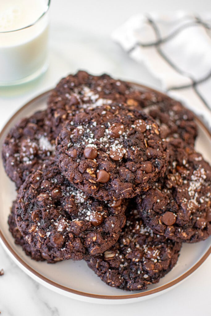 eggless chocolate oatmeal raisin cookies with flaky sea salt on a plate on a marble counter.