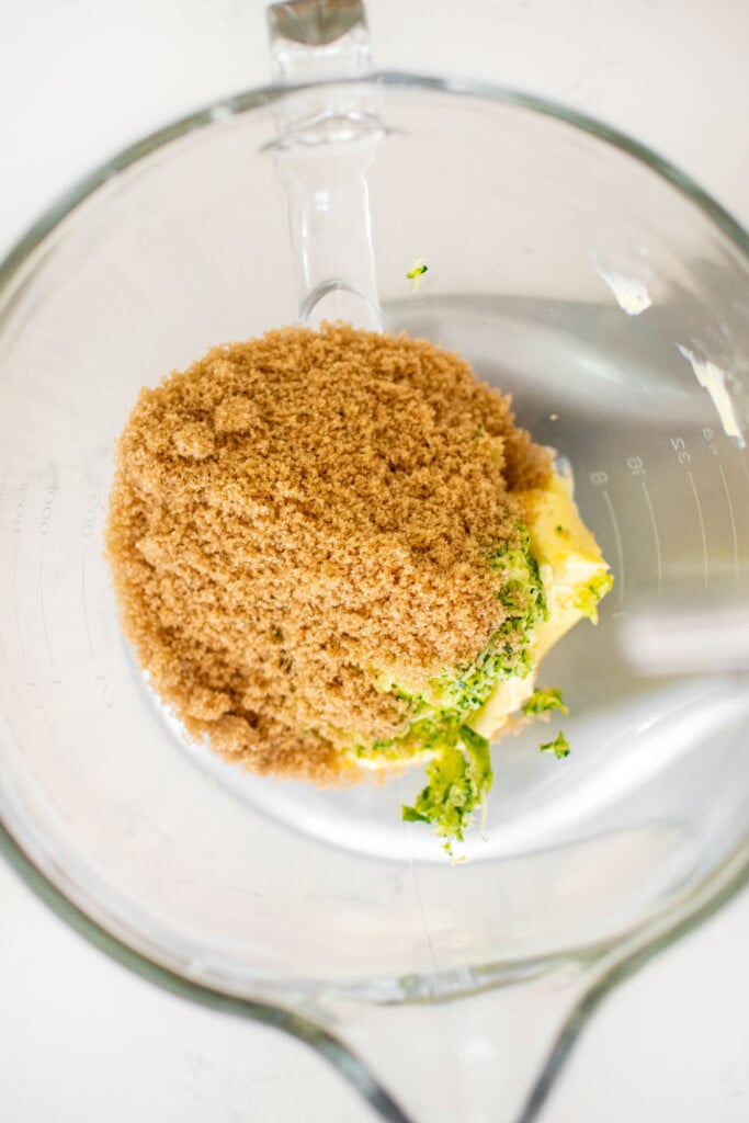 ingredients for eggless strawberry zucchini cake in a glass stand mixing bowl on a white marble counter.