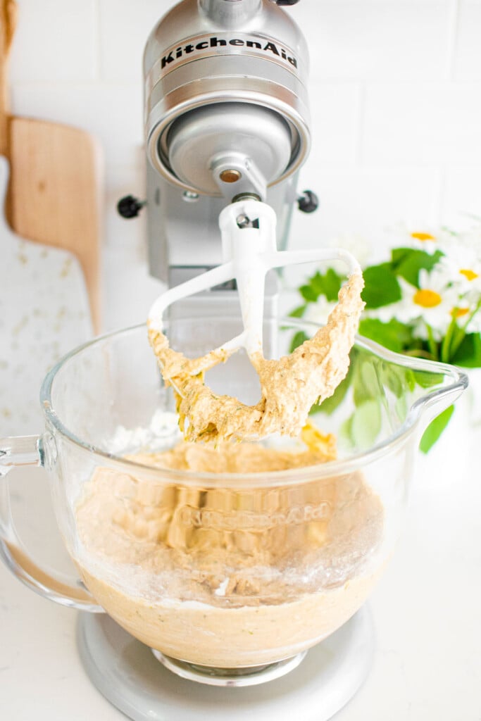 eggless strawberry zucchini cake batter in a stand mixing bowl on a white marble counter with fresh flowers.