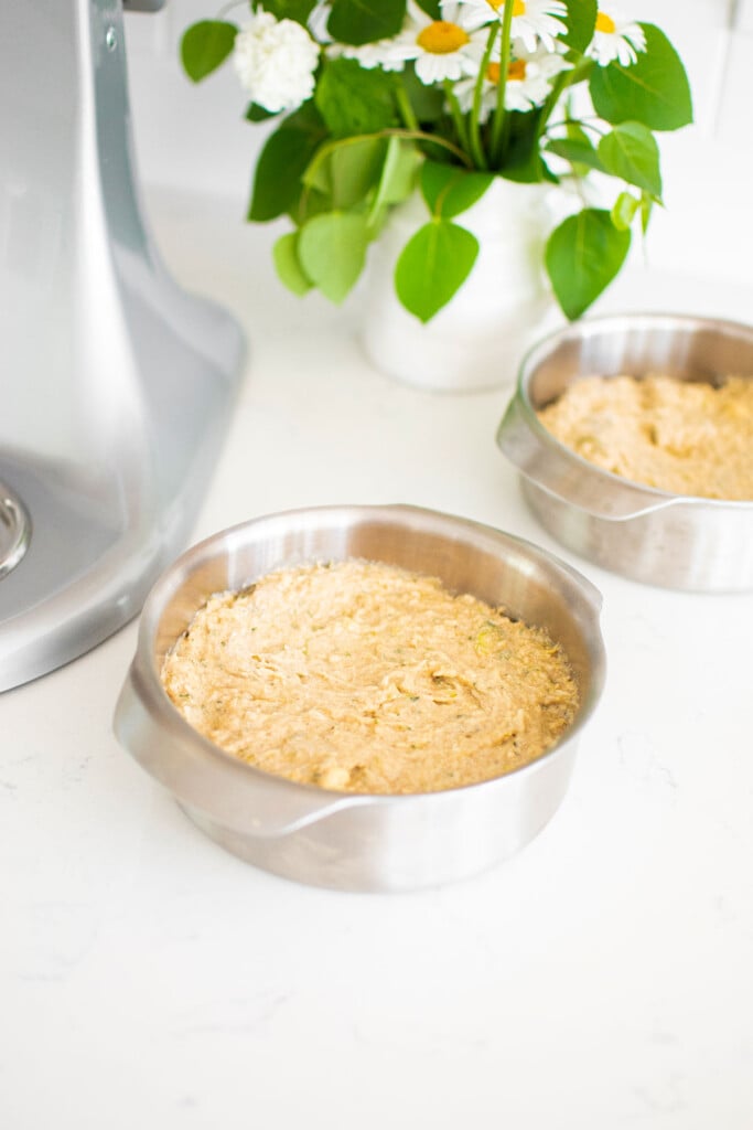 eggless strawberry zucchini cake in cake pans on a white marble counter with fresh flowers.