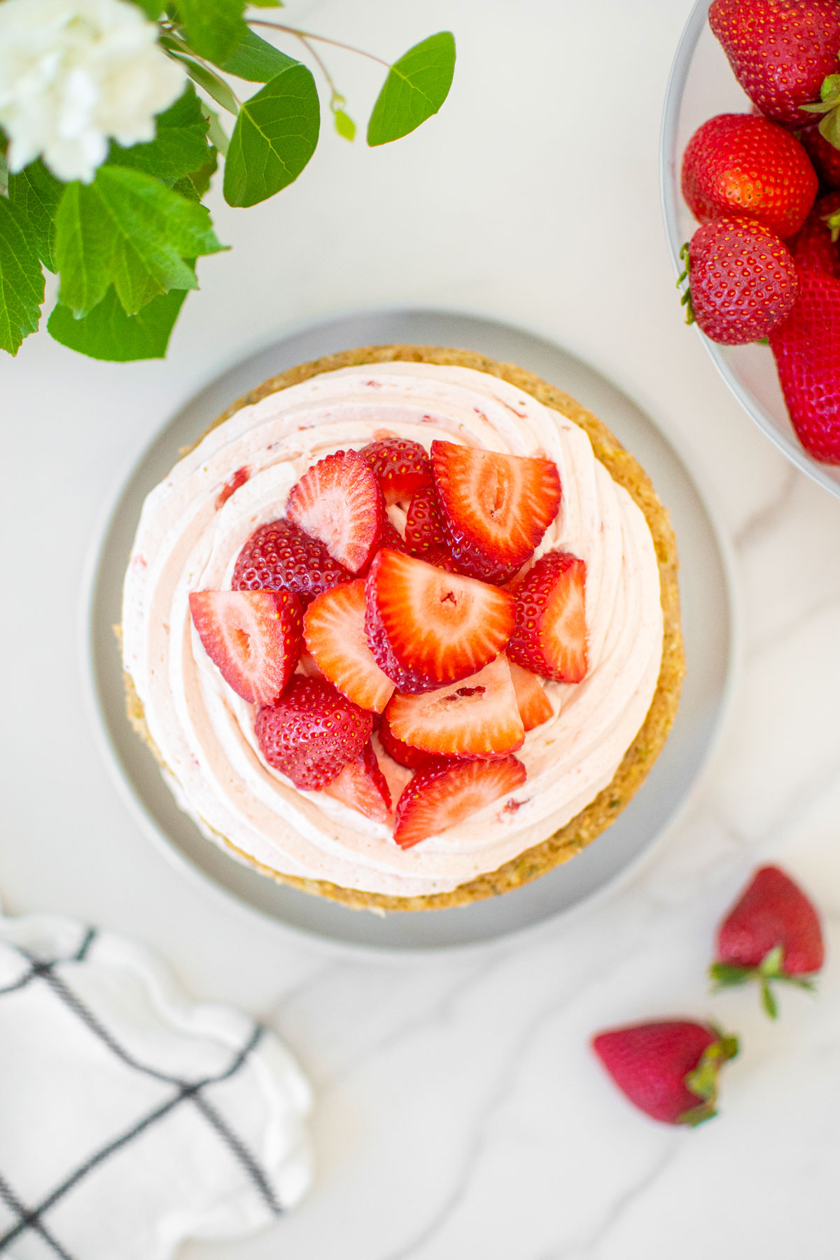 eggless strawberry zucchini cake on a cake plate with fresh strawberries on top on a white marble table with fresh flowers.