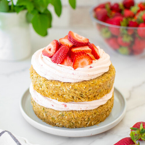 eggless strawberry zucchini naked cake with fresh strawberries on a cake plate on a marble table with flowers.