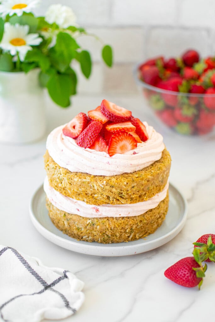 eggless strawberry zucchini naked cake with fresh strawberries on a cake plate on a marble table with flowers.