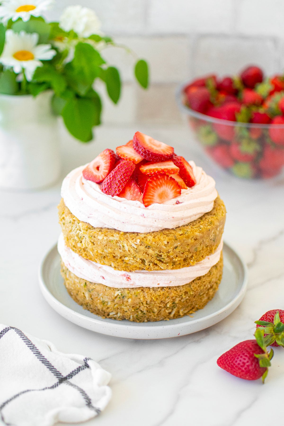 eggless strawberry zucchini naked cake with fresh strawberries on a cake plate on a marble table with flowers.